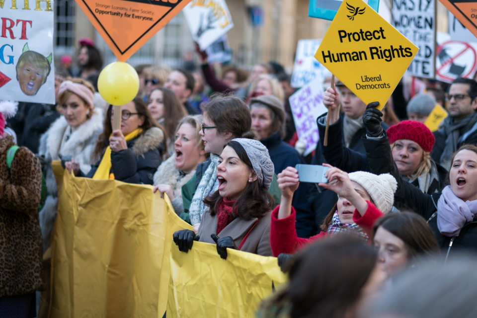 Women stand together chanting while holding a banner at the Women's March against Donald Trump in London, UK (21st January 2017) (Photo credit: Laurence Prax)