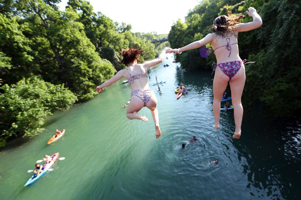 Residents jump off a bridge while swimming, paddle boarding and kayaking in Barton Creek on May 20, 2020 in Austin, Texas. (Photo by Tom Pennington/Getty Images)