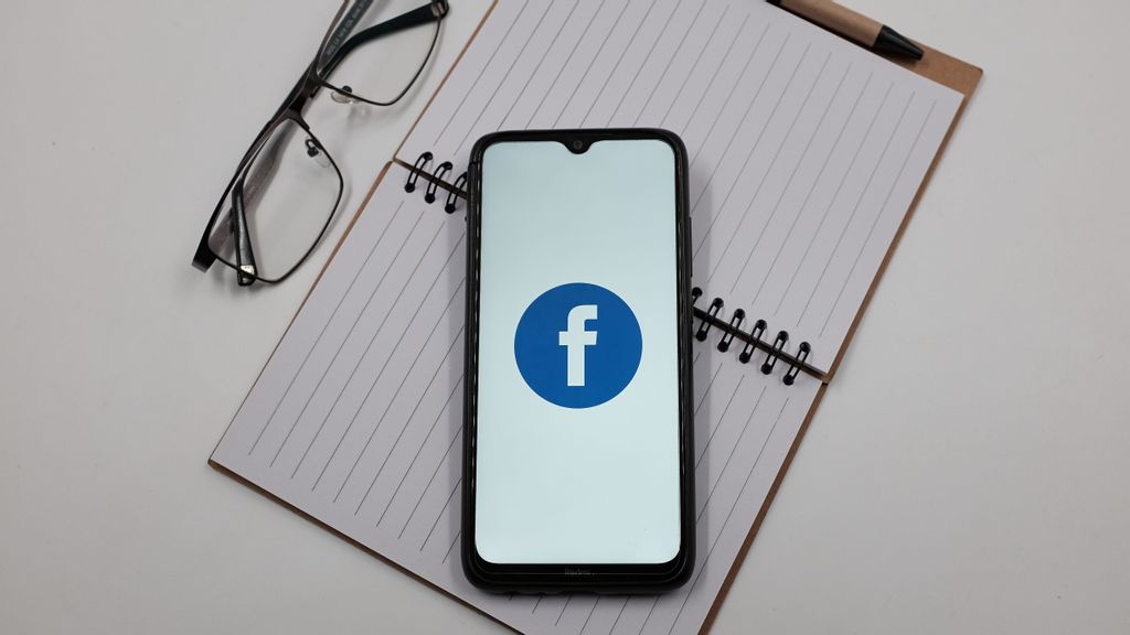 In this photo illustration a Facebook logo is displayed on a smartphone screen above a notebook next to glasses in Athens, Greece on April 4, 2023. Meta Platforms has canceled Jada Pinkett-Smith's show ‘Red Table Talk' due to Meta getting rid of its original programing. NIKOLAS KOKOVLIS/BENZINGA