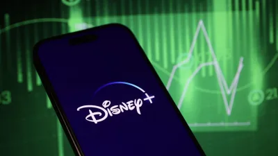 In this photo illustration, logo of Disney+ is displayed on mobile phone screen in front stock exchange screen. Disney stock receive bad ratings from McQuarie Research with negative earnings and political fallouts under the Bob Chapek era. HAKAN NURAL/BENZINGA