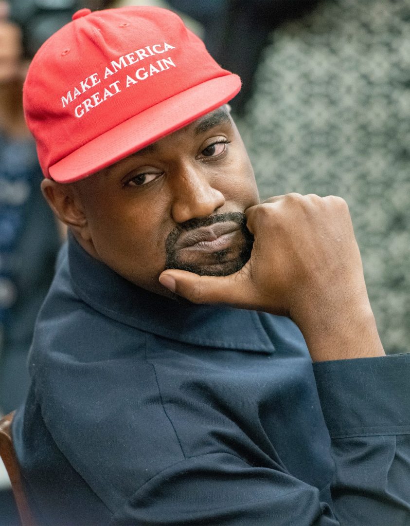 Kanye West wearing a Black shirt and red MAGA hat.